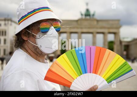 Mature Caucasian LGBT man in Berlin with rainbow fan and ribbon on white summer hat. Rainbow, symbol of LGBTQIA gay pride, diversity. Male activist is Stock Photo