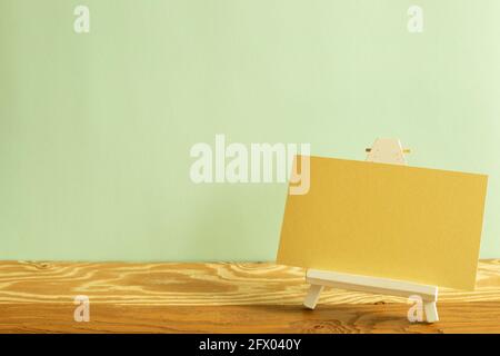 Easel with blank yellow canvas on wooden table. khaki green background Stock Photo