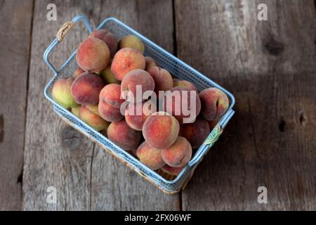 Fresh peaches fruits in basket on dark wooden rustic background, top view. Summer harvest of fruit. Still life. A group of ripe peach. Flat lay vegan food. Copy space. Stock Photo
