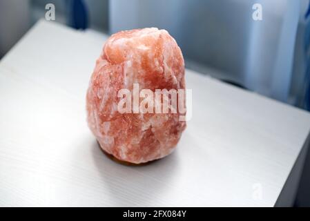 An orange salt lamp stands on a white bedside table Stock Photo