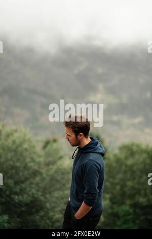Side view thoughtful male hiker standing on mountain summit in highlands in Seville on overcast misty weather Stock Photo