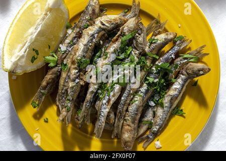 Top view plate of appetizing grilled anchovies served on table with piece of lemon and fresh herbs in restaurant Stock Photo