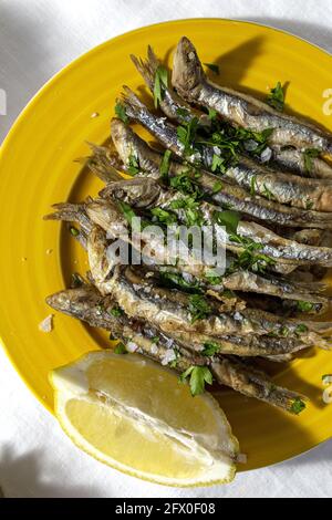 Top view plate of appetizing grilled anchovies served on table with piece of lemon and fresh herbs in restaurant Stock Photo