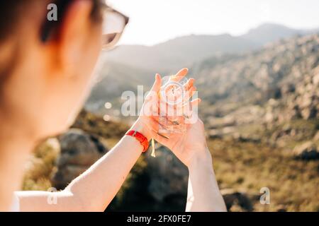 Crop anonymous female traveler holding modern compass in hand while standing on mountain slope on sunny day Stock Photo