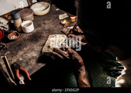 From above cropped anonymous mature ethnic man working at weathered desk in craft workshop Stock Photo