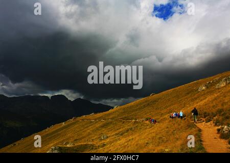 Wanderer auf einer Alm Wiese mit Wanderweg mit Gewitter Wolken  in der sommerlichen Bergwelt der Dolomiten am Langkofel in Südtriol in Italien Stock Photo