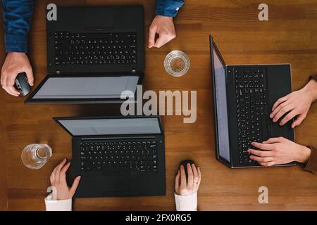 Four unrecognizable people working with their laptops on wooden table Stock Photo