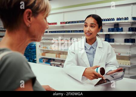 Female pharmacist guiding customer with tablets by showing something on digital tablet Stock Photo