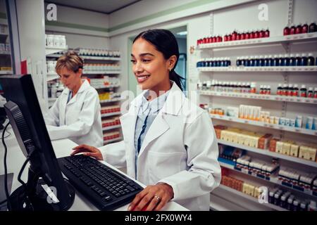 Young female pharmacist using computer with senior colleague using digital tablet in chemist Stock Photo