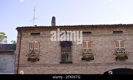 The facade of a brick building with gold-colored shutters and ornamental plants (Marche, Italy, Europe) Stock Photo