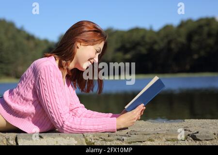 Side view portrait of a happy woman reading a book in a lake in the mountain Stock Photo