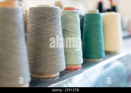 Receding row of cashmere wool on conical spools in shades of green, grey and white at a knitwear factory with focus to a reel of green yarn in the cen Stock Photo