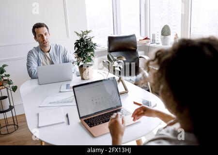 Young and ambitious team of office employees creative partners working together at home on project look at laptop discuss task, share ideas and Stock Photo
