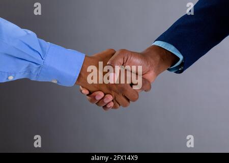 Mid section of two businessmen shaking hands against grey background Stock Photo