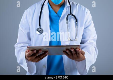 Mid section of female doctor holding digital tablet against grey background Stock Photo
