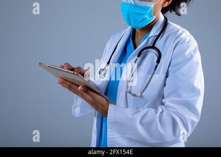 Mid section of female doctor wearing face mask using digital tablet against grey background Stock Photo