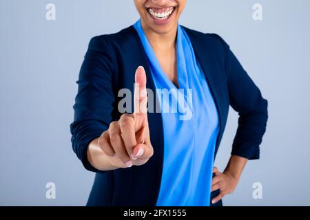 Mid section of businesswoman smiling while touching invisible screen against grey background Stock Photo