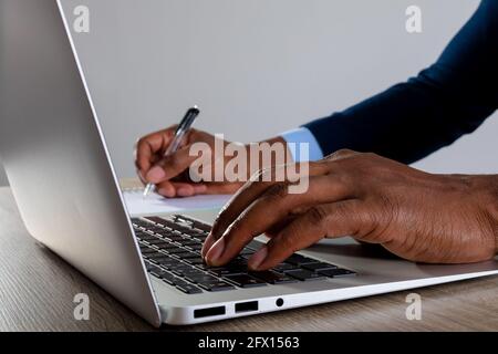 Close up of businessman using laptop and taking notes against grey background Stock Photo