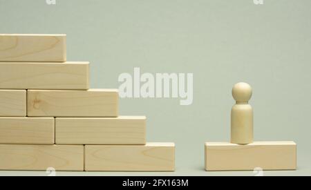 wooden figurine of a man stands on a staircase made of blocks on the first step. The concept of achieving the set goals in business, career growth, st Stock Photo