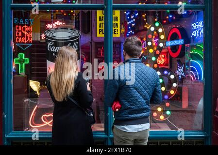 London, UK.  25 May 2021. Passers by view “Electric City” an exhibition in Leadenhall Market of neon and set pieces made for film by Gods Own Junkyard, which has worked on film sets for over 40 years. Founder, Chris Bracey passed away in 2014 and the business has since been run by his wife Linda and sons Matthew and Marcus, all neon makers and designers. On show 26th May to 31st July is neon signage from Stanley Kubrick’s Eyes Wide Shut, Judge Dredd, Batman, Tomb Raider, Charlie and the Chocolate Factory and The Dark Knight.  Credit: Stephen Chung / Alamy Live News Stock Photo