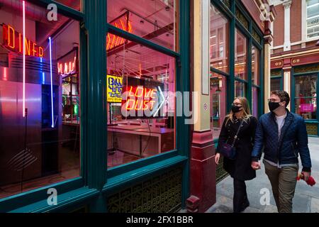 London, UK.  25 May 2021. Passers by view neon from Judge Dredd, part of “Electric City” an exhibition in Leadenhall Market of neon and set pieces made for film by Gods Own Junkyard, which has worked on film sets for over 40 years. Founder, Chris Bracey passed away in 2014 and the business has since been run by his wife Linda and sons Matthew and Marcus, all neon makers and designers. On show 26th May to 31st July is neon signage from Stanley Kubrick’s Eyes Wide Shut, Judge Dredd, Batman, Tomb Raider, Charlie and the Chocolate Factory & The Dark Knight.  Credit: Stephen Chung / Alamy Live News Stock Photo
