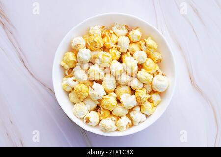 A small white bowl of caramelized popcorn. Light marble background. Sweet popcorn close up. Stock Photo