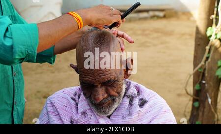 01 January 2021- Reengus, Sikar, India. Indian rural shot, traditional barber shaving old man in village of rajasthan, India. Stock Photo
