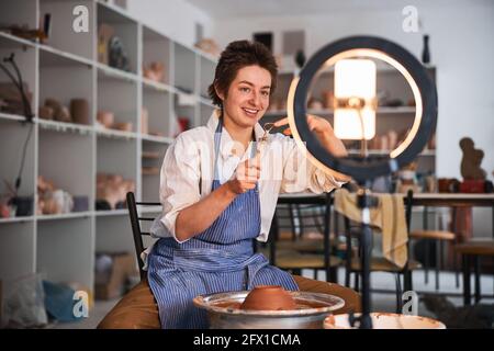 Potter showing loop tool at mobile phone near pottery wheel Stock Photo