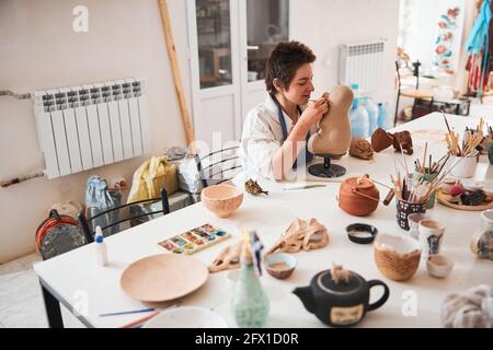Potter involved in carving the face of clay model Stock Photo