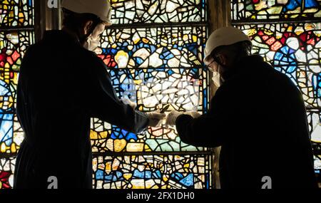 Conservator Matthew Nickels (left) and Master Glazier Tony Cattle (right) from York Glaziers Trust removed a stained glass window panel at the start of a new five year, £5m project to conserve York Minster's South East Transept and its medieval St Cuthbert Window. Picture date: Tuesday May 25, 2021. Work is being undertaken by York Glaziers Trust to remove stained glass panels from the window, which is nearly 600-years-old and one of the largest surviving narrative windows in the world. The project involves major conservation and restoration works to both the stained glass and stone elements o Stock Photo