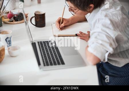 Focused worker bending over notepad while writing with pencil Stock Photo