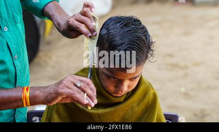 Indian barber working on the village streets in a sunny day. A barber cutting hair of Indian boy during lockdown in India. Stock Photo