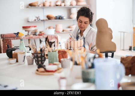 Woman ceramist involved in pot painting at workshop table Stock Photo