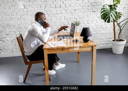 African american male freelancer is having a conversation with colleague, discussing project. Successful businessman is using smartphone, working Stock Photo