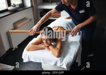 Adorable pretty lady with towel relaxing at the massage manual therapy with wooden tool in health clinic Stock Photo
