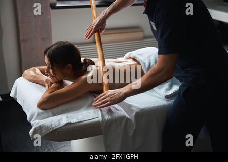 Beautiful Caucasian young woman under the towel relaxing and resting while getting manual therapy with massager in wellness center Stock Photo