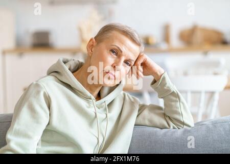 Thoughtful beautiful mature woman in casual clothes dreaming and thinking while sitting relaxing on sofa, spending leisure time at home. Focus on senior female. Senior people Stock Photo