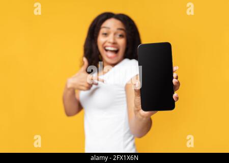 Amazing message. Surprised african american lady showing smartphone with blank screen over yellow background Stock Photo