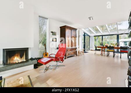 Big open plan room with dining area and red armchair at fireplace and vintage wooden cupboard in luxury house Stock Photo