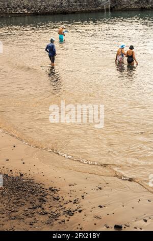 People enter the water under a strange light caused by smoke from a forest fire blocking the sun, Playa San Juan, Tenerife, Canary Islands, Spain Stock Photo