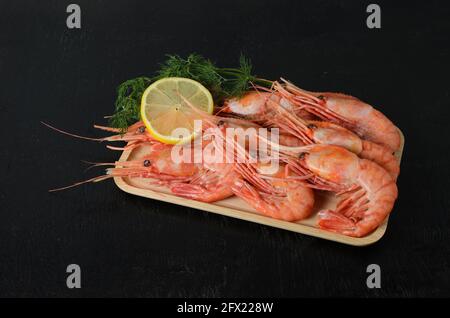 Boiled shrimps in a shell with dill and lemon in a wooden bowl on a dark wooden background. Selective focus. Stock Photo
