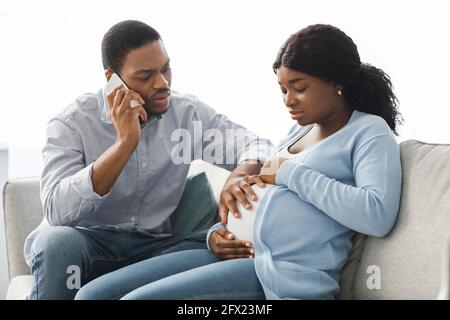 Worried black husband calling doctor while wife having labor pains Stock Photo