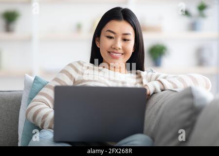 Remote Work. Portrait Of Smiling Young Asian Lady Using Laptop At Home Stock Photo