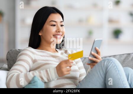 Happy Asian Woman With Smartphone And Credit Card Using Online Banking App Stock Photo