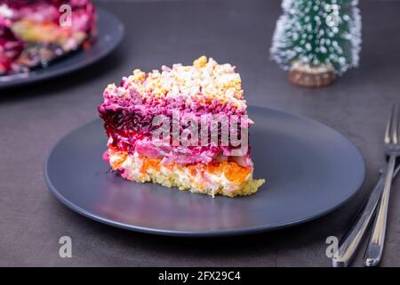 Herring salad under a fur coat. Traditional Russian multilayered salad from herring, beets, potatoes, carrots and eggs. Small Christmas tree. Close-up Stock Photo