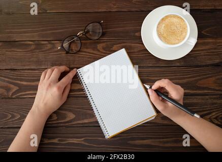 Goals or plan writing concept. Woman with empty notebook and cup of coffee, sitting on dark wooden table, top view Stock Photo