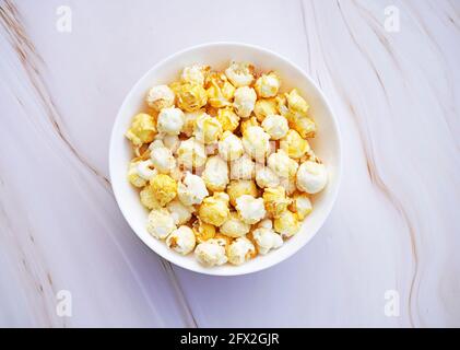 A small white bowl of caramelized popcorn. Light marble background. Sweet popcorn close up. Stock Photo