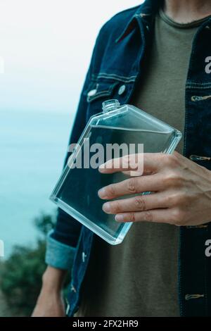 a young man, wearing a denim jacket and a casual green t-shirt, is about to drink from a rectangular reusable water bottle Stock Photo