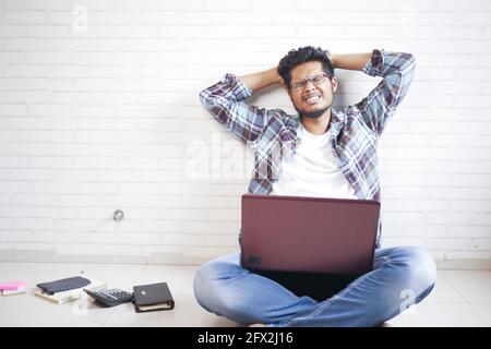 sad man working on laptop at home while sited on floor  Stock Photo