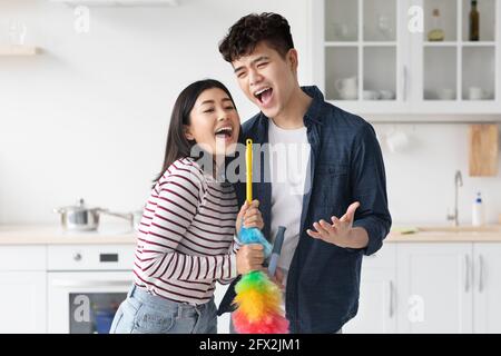 Funny asian couple singing songs while cleaning kitchen Stock Photo